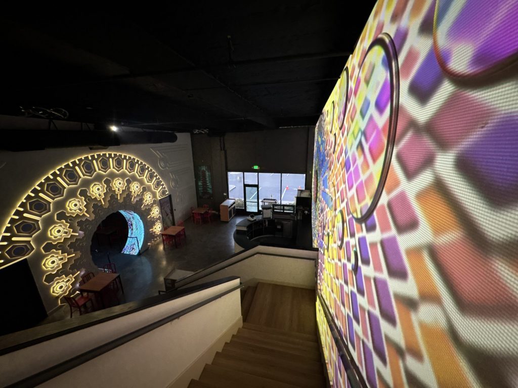 The portal of wonder on the left and projection mapped wall on the right in the cafe space with stairs leading up to the event space.